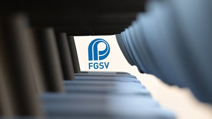 FGSV-Logo zwischen unscharfen Reihen von grauen und schwarzen Stühlen oder Bauteilen im Vordergrund.